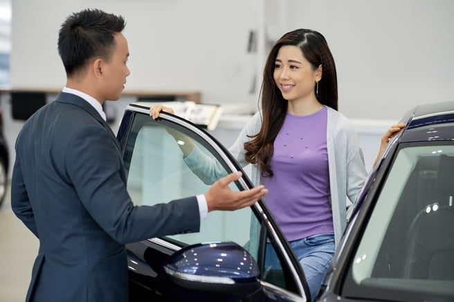 Asian Car Salesman Speaks to Woman Entering Car