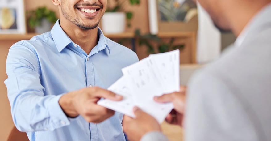 a happy young adult handing over multiple paper checks to a business