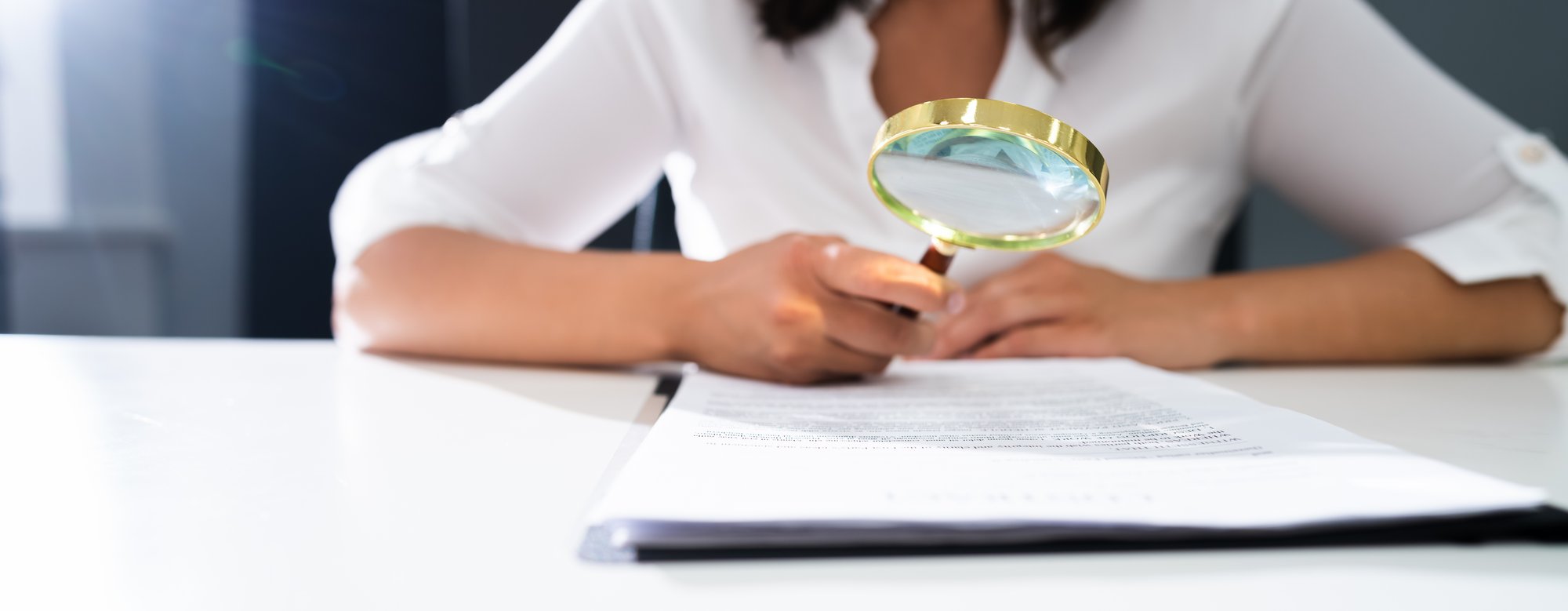 Businessperson using a magnifying glass for a closer look at documents on a desk.