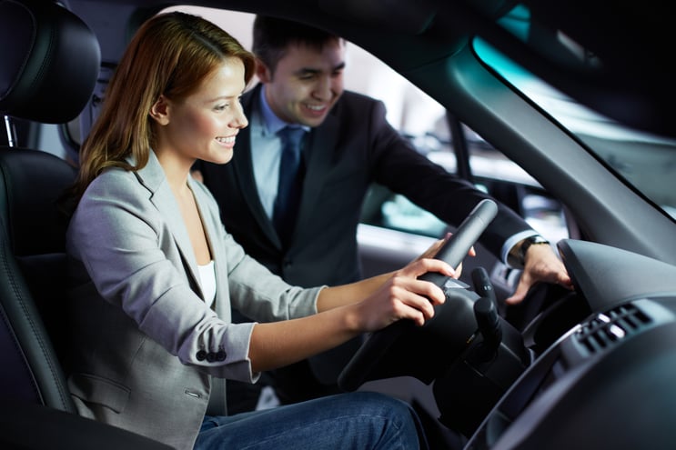 Car salesman smiling with a happy woman customer in the driver's seat of a car