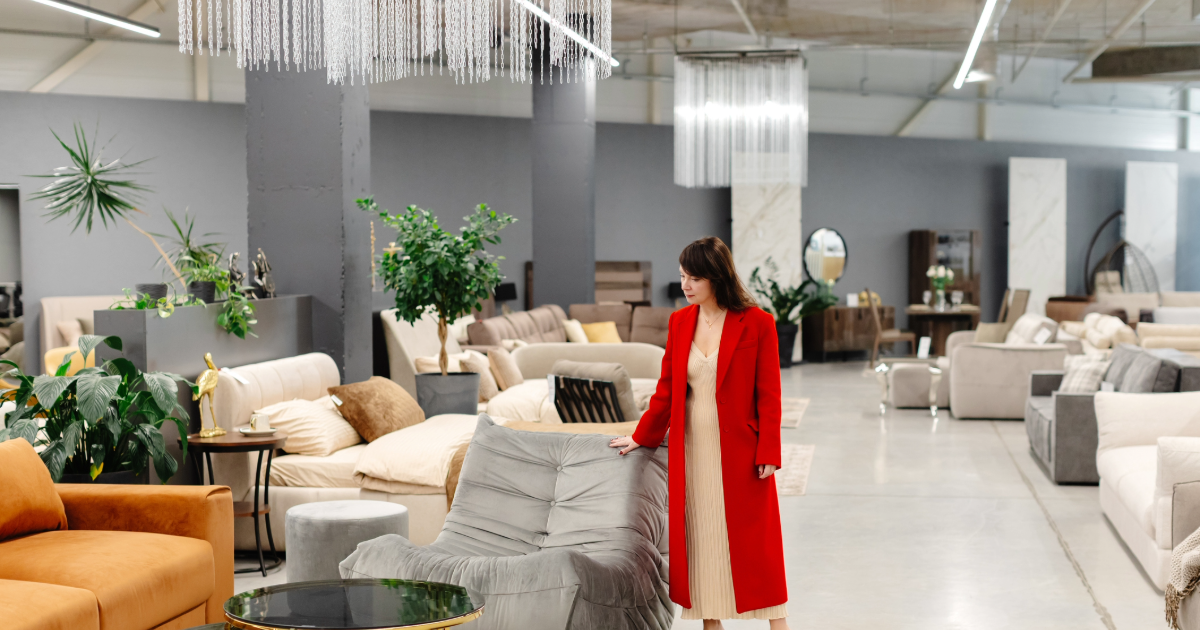 A woman in a red coat browsing modern living room furniture displays inside a spacious, high-end retail furniture store showroom.