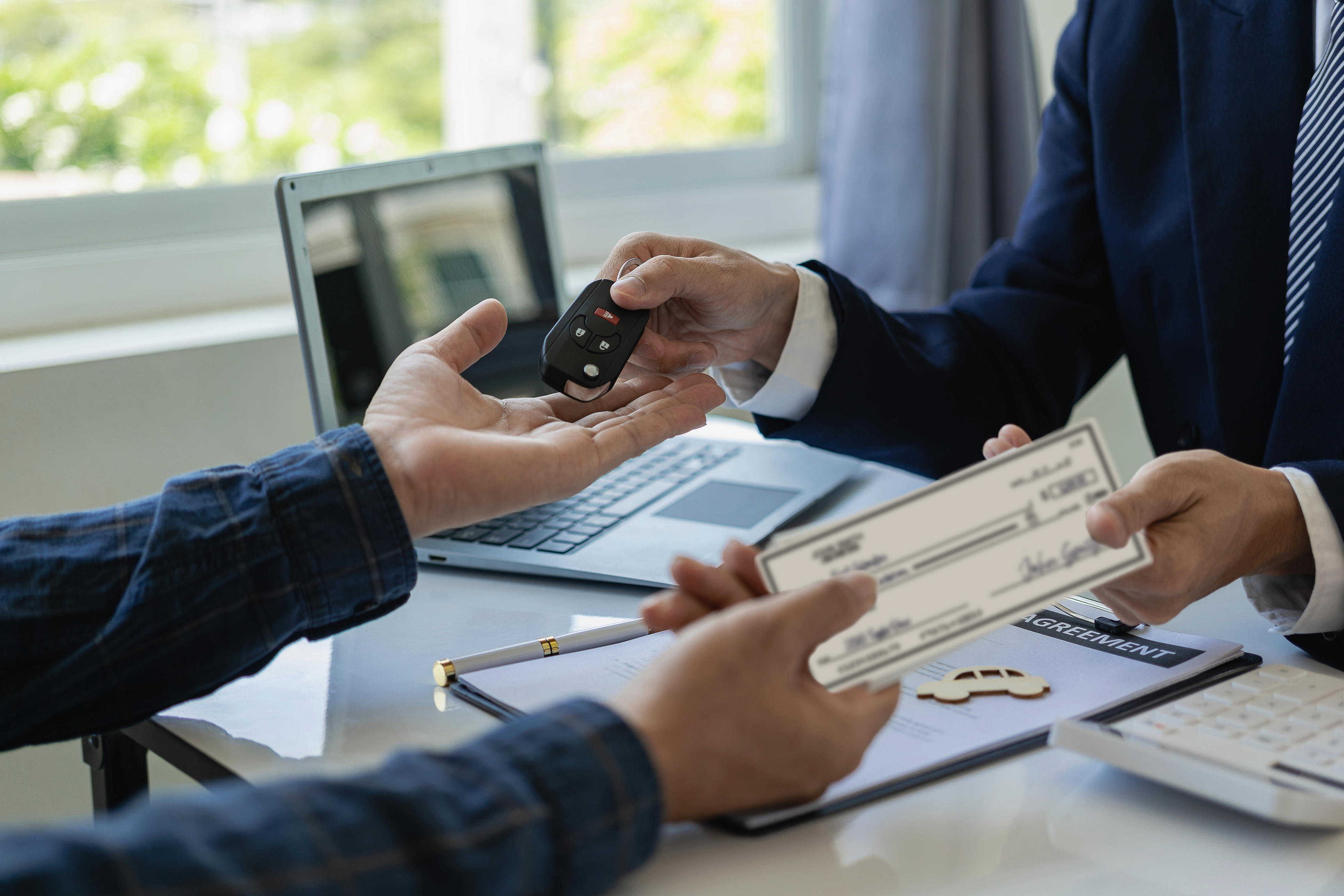 Hands of a consumer exchanging a personal check for car keys with hands from a dealership sales person.