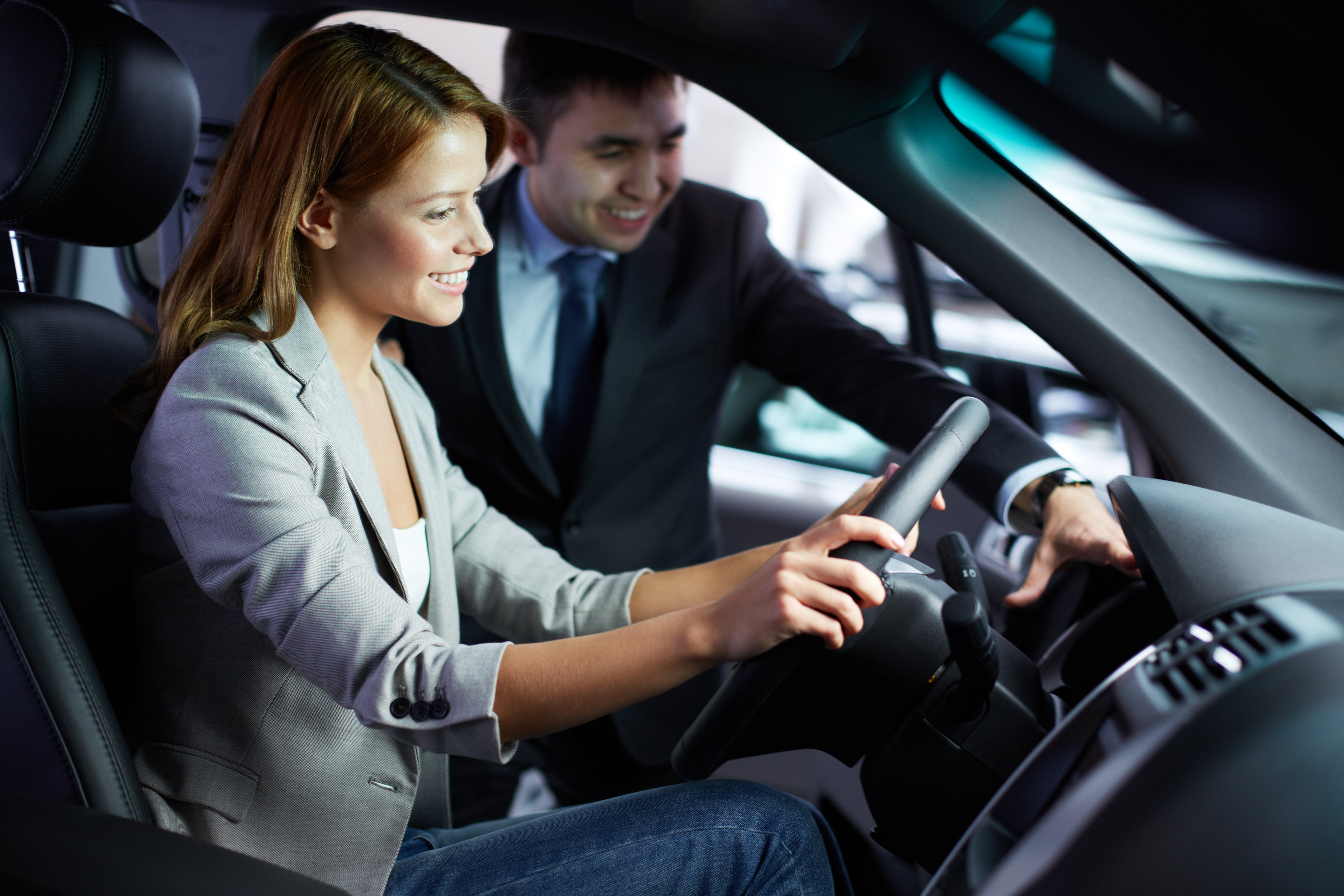 Car salesman smiling with happy female customer sitting in the driver's seat of a car.